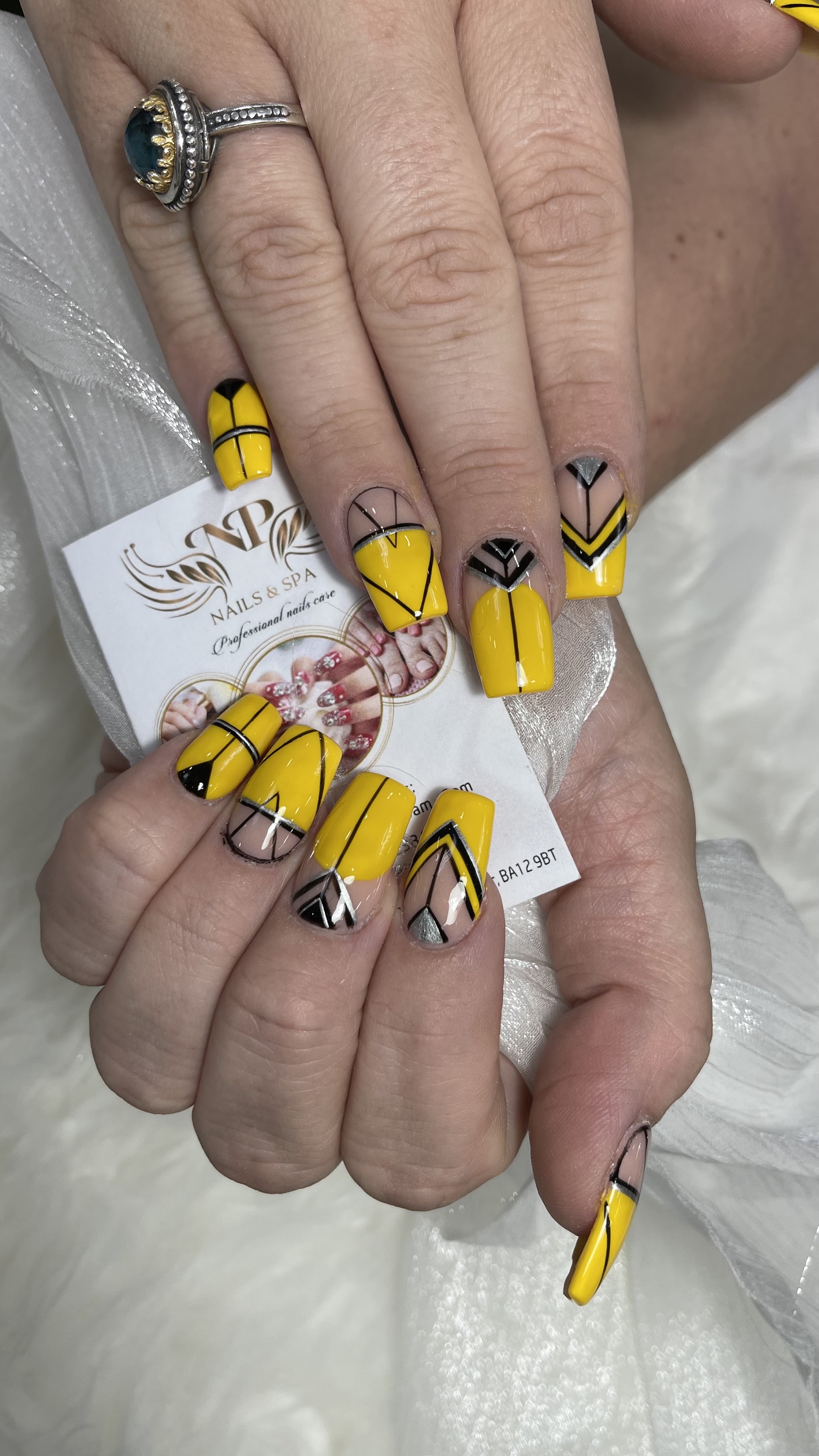 Yellow and black geometric nails holding an NP Nails & Spa card