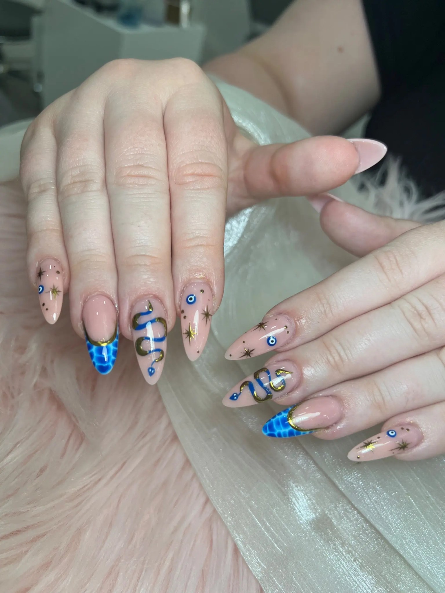 Nude almond nails with blue evil-eye and snake art